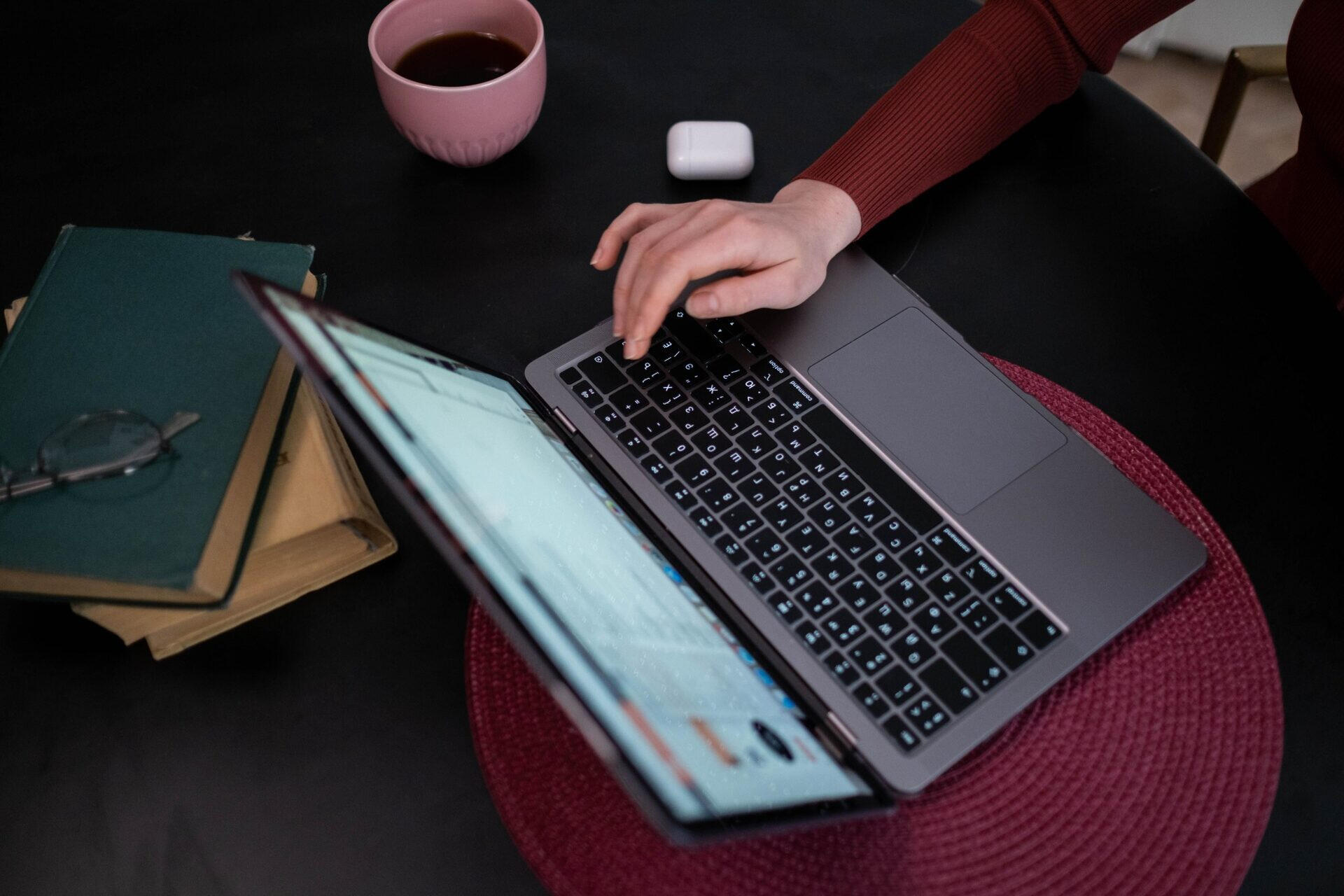 Hand typing on a laptop beside a stack of notebooks and a coffee cup.